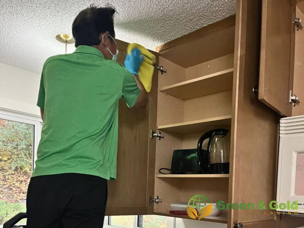 A man is cleaning a cabinet in the kitchen.